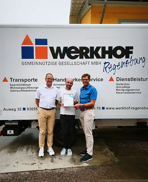 Harald Sentner vom LBT überreicht Peter Astashenko und Thomas Arnold die Urkunde für 20 Jahre Mitgliedschaft im Landesverband Bayerischer Transport- und Logistikunternehmen. Im Hintergrund steht ein Lkw des Werkhofs Regensburg.
