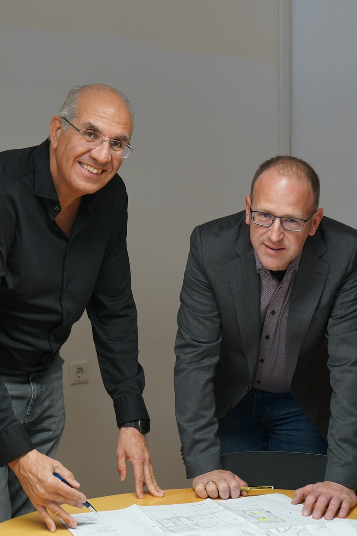 Bereichsleiter Josef Pfeiffer (links im Bild) und Werkhof‑Geschäftsführer Peter Astashenko stehen an einem Tisch, betrachten einen Plan und schauen in die Kamera.