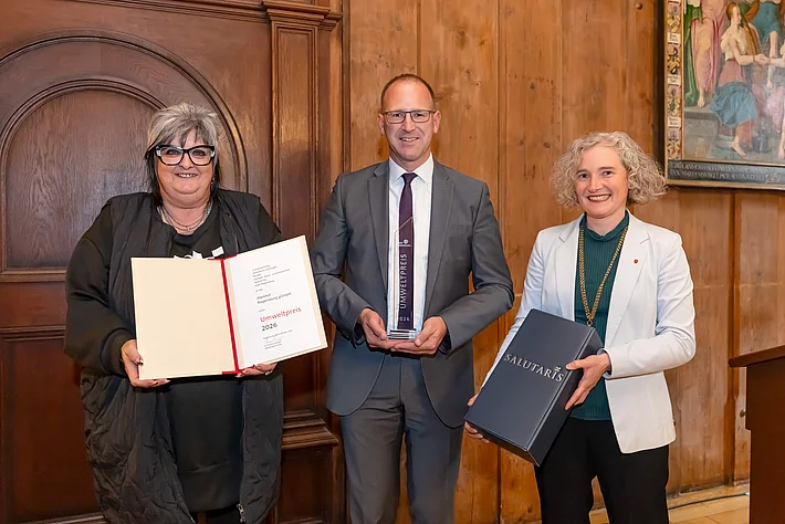 Gebrauchtwarenhausleiterin Angela Weber präsentiert die Urkunde zum Umweltpreis der Stadt Regensburg. Werkhof-Geschäftsführer Peter Astashenko hält die Auszeichnung in den Händen. Bürgermeisterin Dr. Helene Sigloch überreicht eine Flasche Salutaris-Wein aus Regensburg.