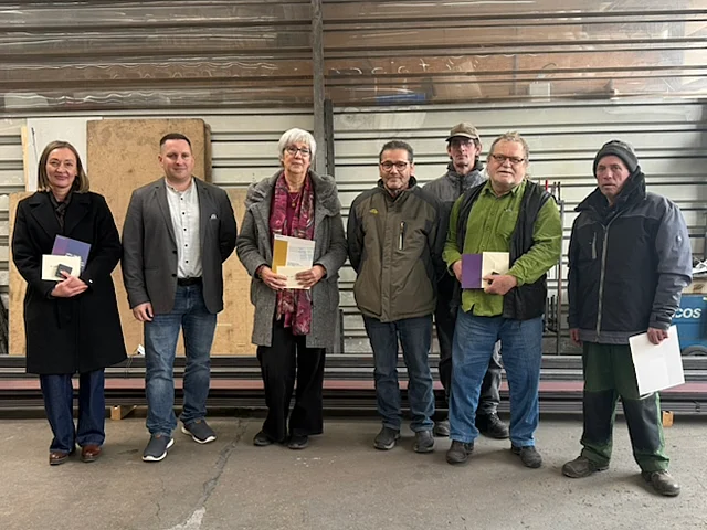 Geschäftsführer Dr. Michael Reil steht mit mehreren langjährigen Mitarbeitenden zusammen. Die Gruppe posiert lächelnd für ein Foto während einer Ehrung.“