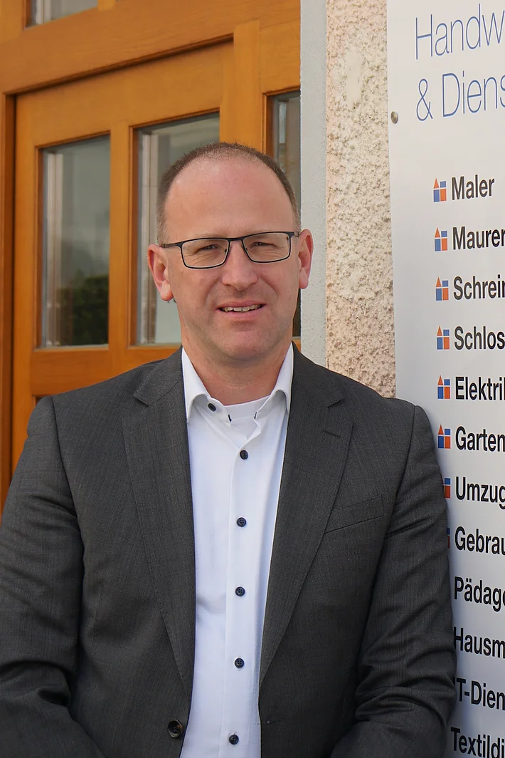 Geschäftsführer Peter Astaschenko lehnt an der Außenwand des Werkhof Regensburg, im Hintergrund ist ein Schild mit den Gewerken des Werkhofs teilweise sichtbar.