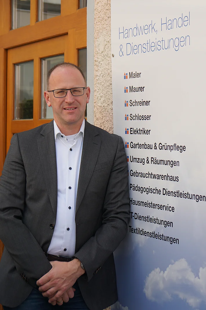 Geschäftsführer Peter Astaschenko lehnt an der Außenwand des Werkhof Regensburg, im Hintergrund ist ein Schild mit den Gewerken des Werkhofs teilweise sichtbar.