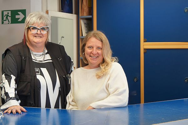 Die Verkaufsleiterin Gebrauchtwarenhaus Regensburg steht mit der Bereichsleiterin Gebrauchtwarenhäuser im Gebrauchtwarenhaus Regensburg an der Kasse. Beide blicken freundlich in die Kamera.