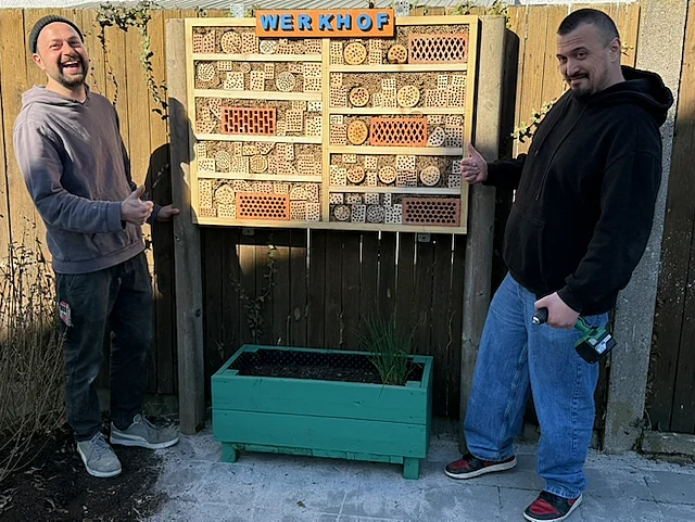 Zwei Personen präsentieren ein selbstgebautes Insektenhotel aus Holz.