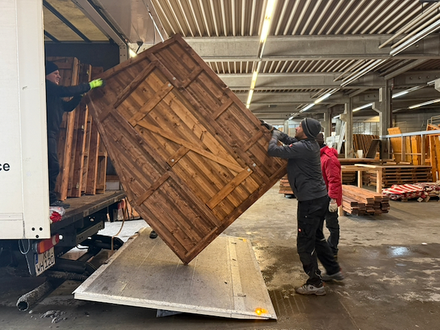Ein Mitarbeiter übergibt ein großes Budenteil vom LKW an zwei weitere Kolleginnen und Kollegen im Lager.